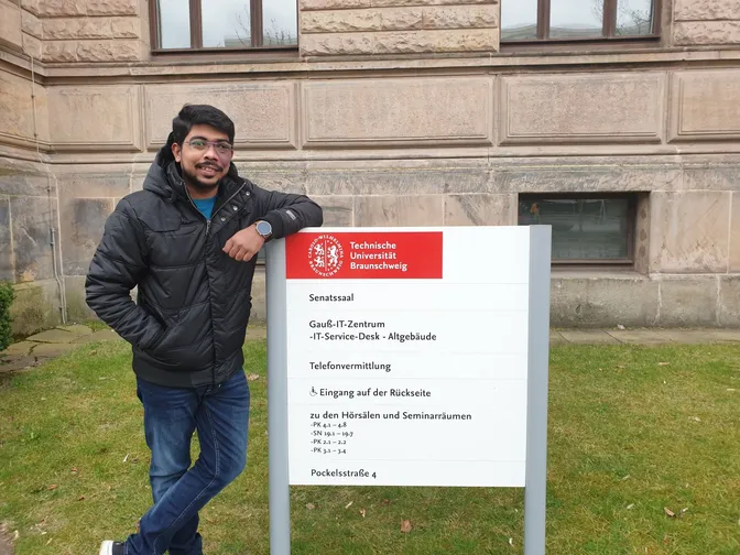 Himanshu Kumar standing beside a Technische Universität Braunschweig sign